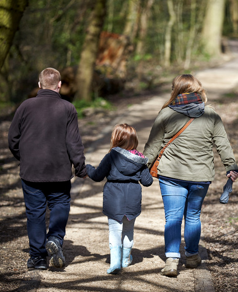 far, mor og datter på udflugt i skov. Man ser dem bagfra, barnet i mellem forældrene